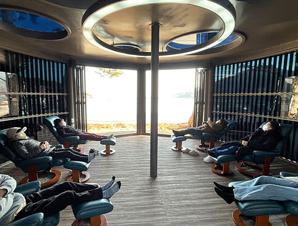 나무로된 테라스에 리클라이너 의자가 여러대 배치되어 있고 그앞으로 파란 바다가 보이는 소리치유관 모습